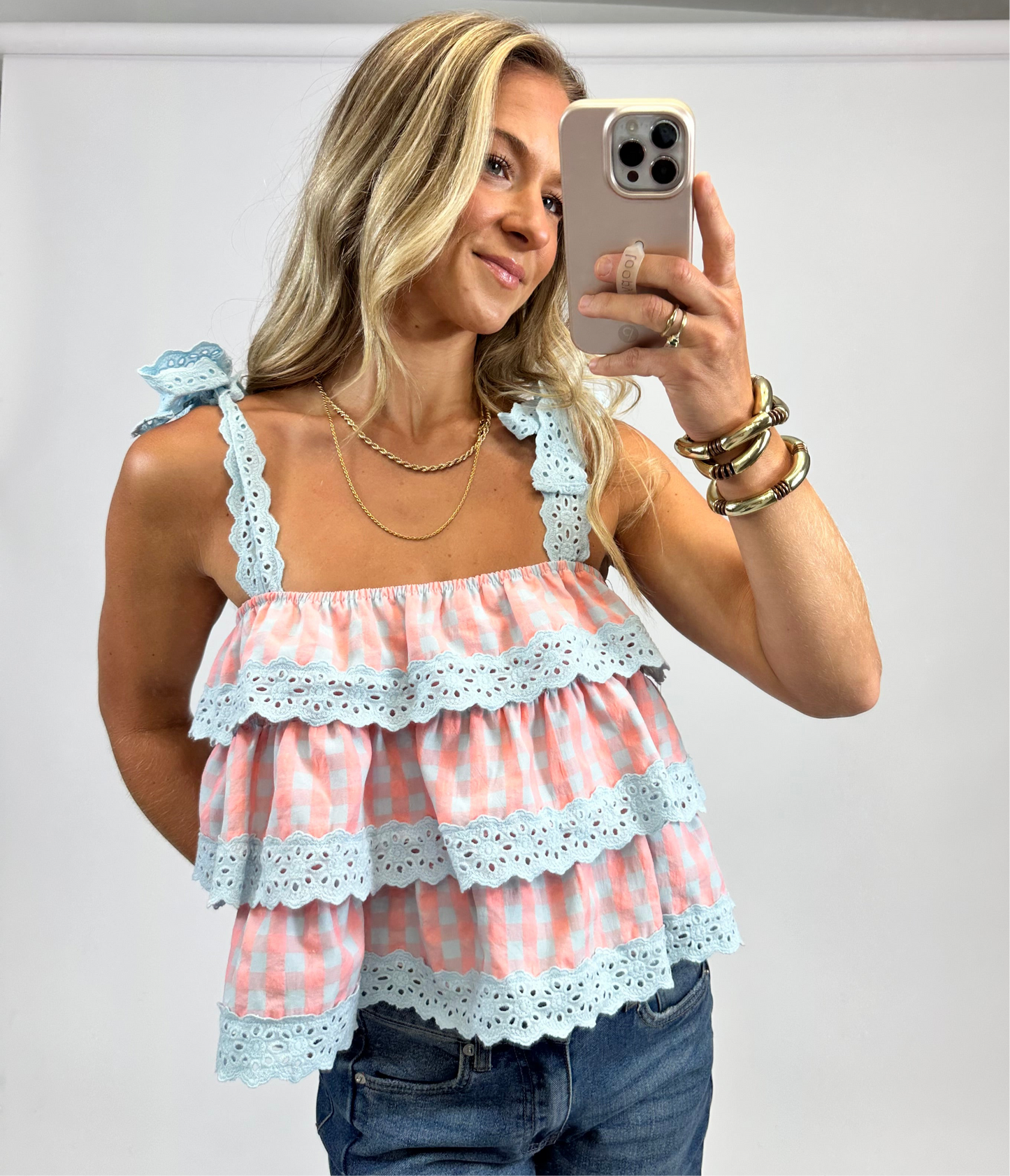 Model wearing the Tula Tank Top in coral and blue gingham with ruffle tiers and tie-shoulder straps from August Moon Boutique