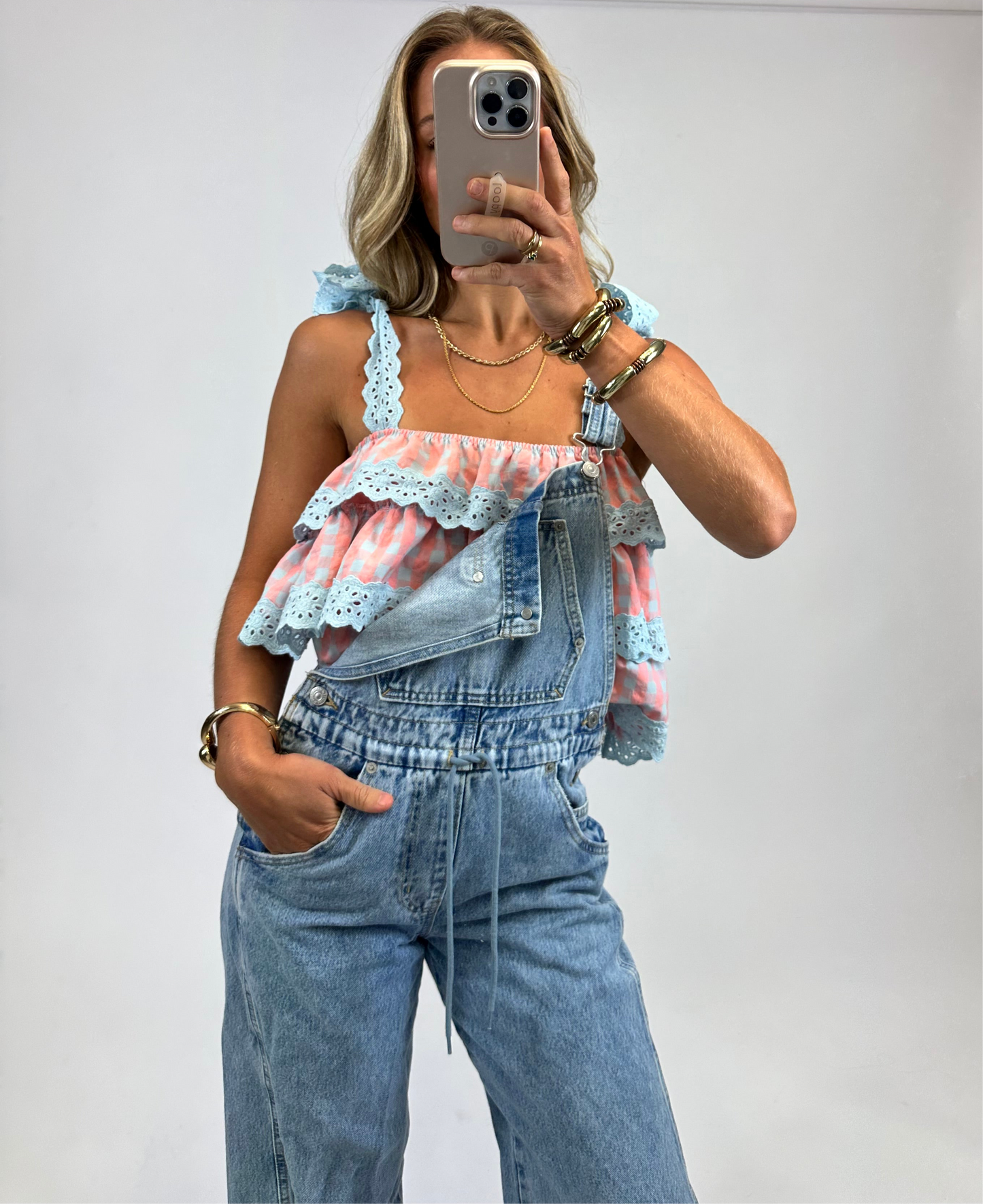 Model wearing the Tula Tank Top in coral and blue gingham with ruffle tiers and tie-shoulder straps from August Moon Boutique